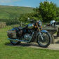 A Royal Enfield Classic 350 Reborn with canvas panniers parked by a bench in the sunlight