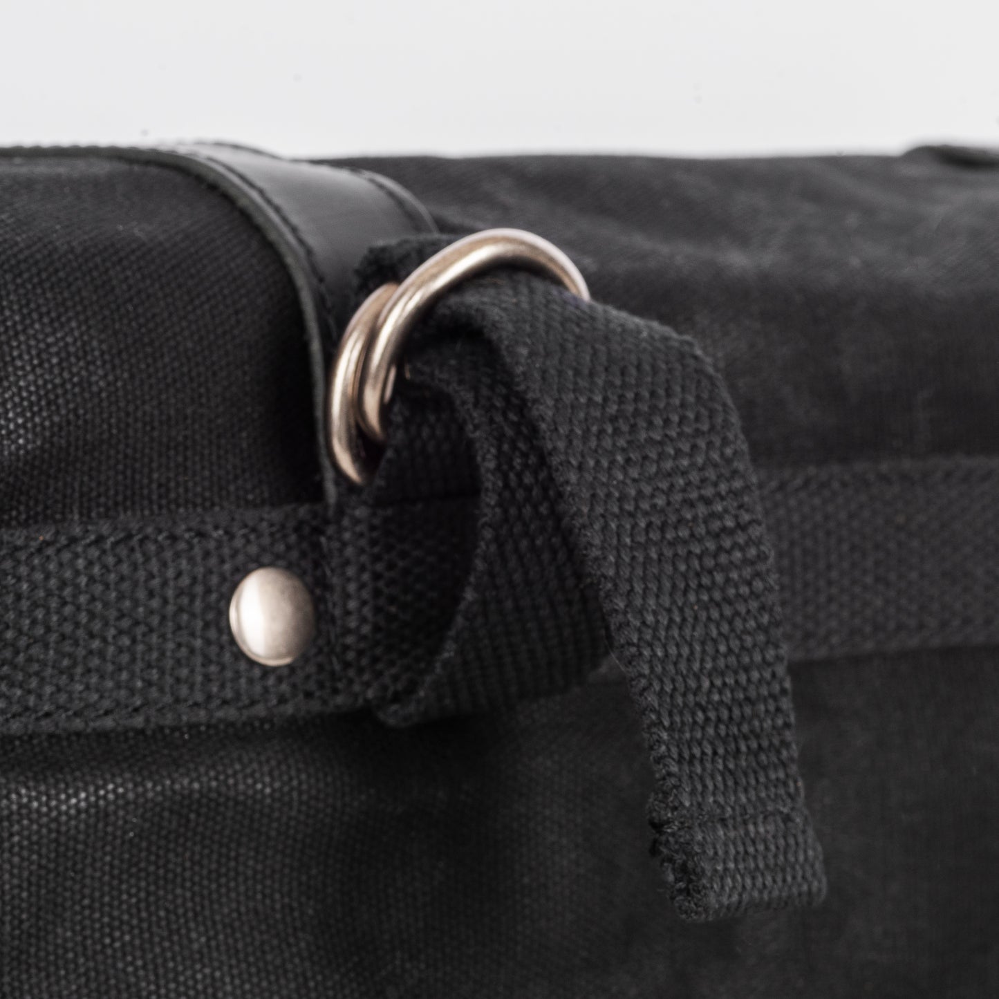 A black waxed canvas motorcycle pannier bag with attachment hoops