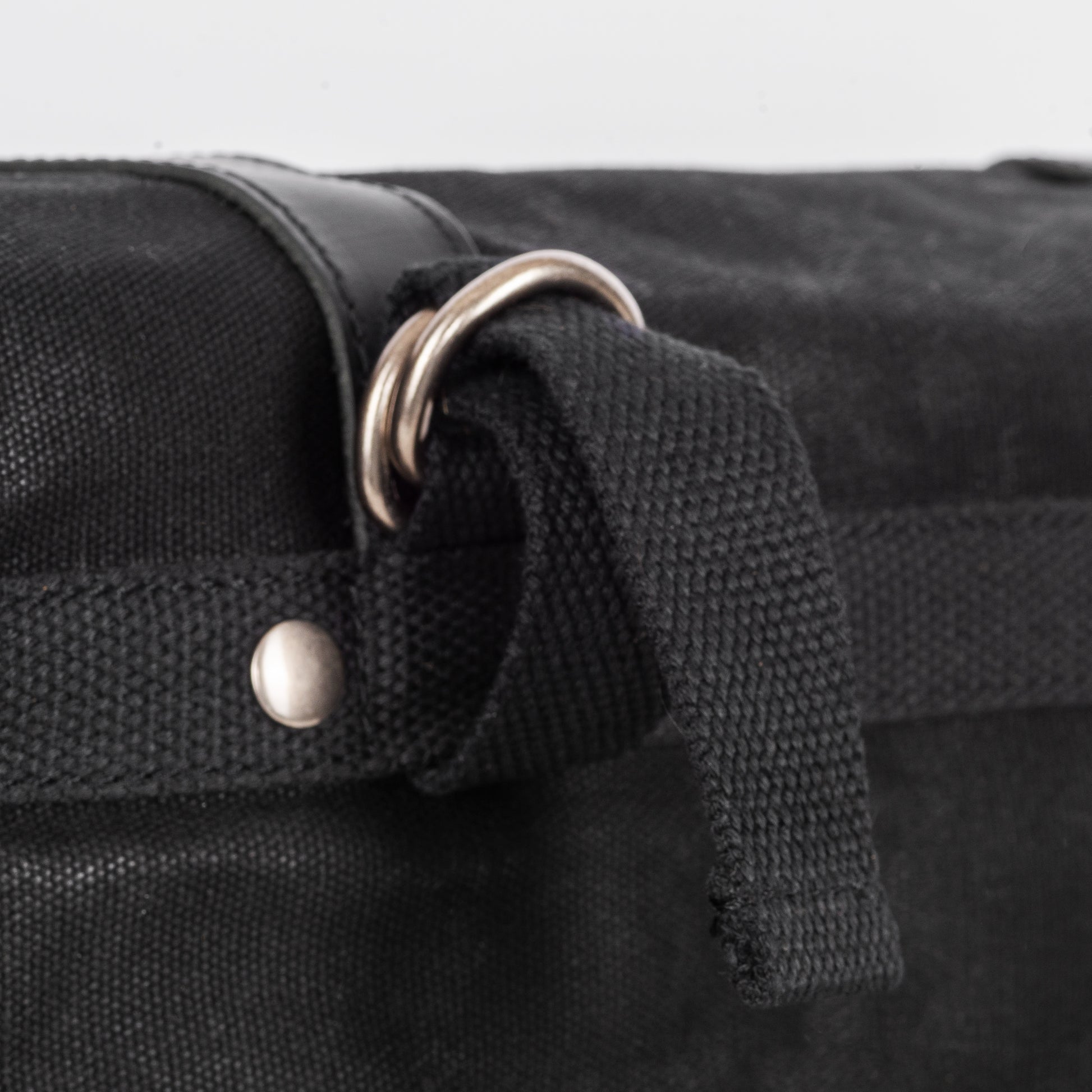 A black waxed canvas motorcycle pannier bag with attachment hoops
