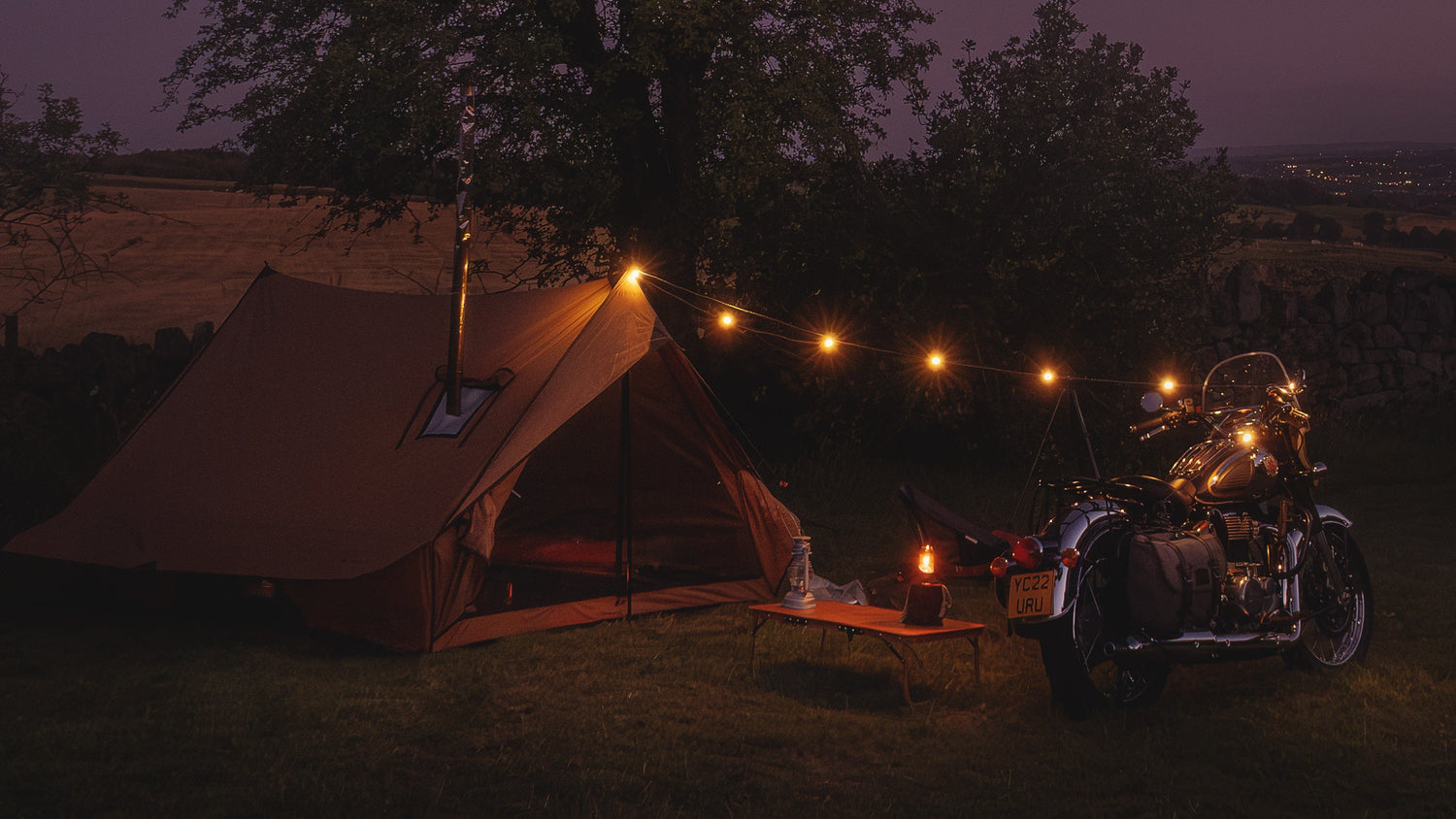 Motorcycle camping with a tent with string lights and a Royal Enfield Classic 350 near a tree at night